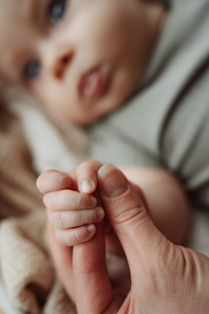 Baby mit blauen Augen umgreift den Finger eines Elternteils, weicher heller Hintergrund